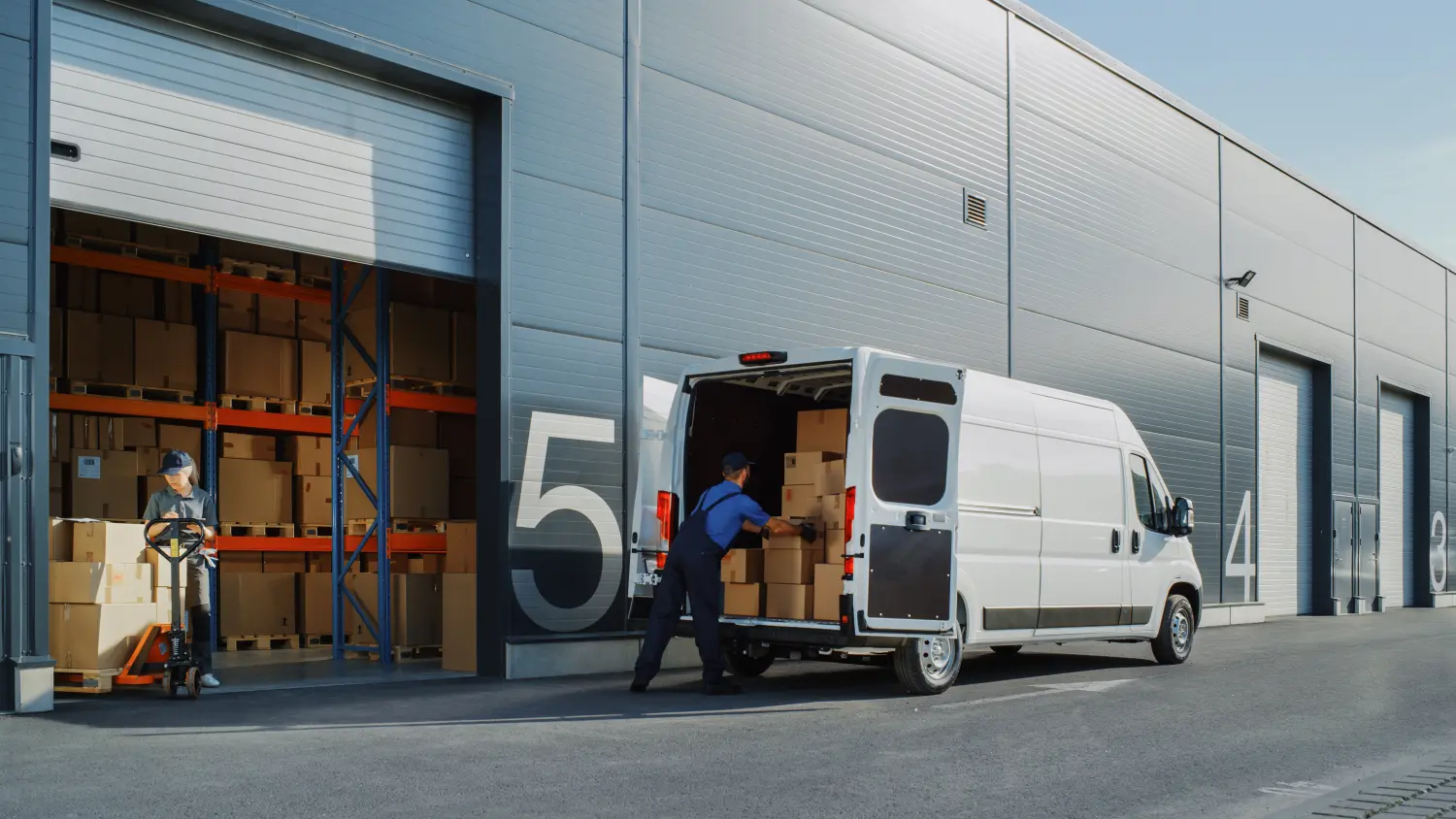 Außerhalb des Lagers eines Logistikeinzelhändlers: Eine Managerin benutzt einen Tablet-Computer und eine Arbeiterin belädt einen Lieferwagen mit Kartons.